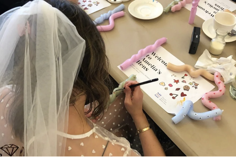 Bride in a veil painting a pastel bendy candle at a hen party workshop