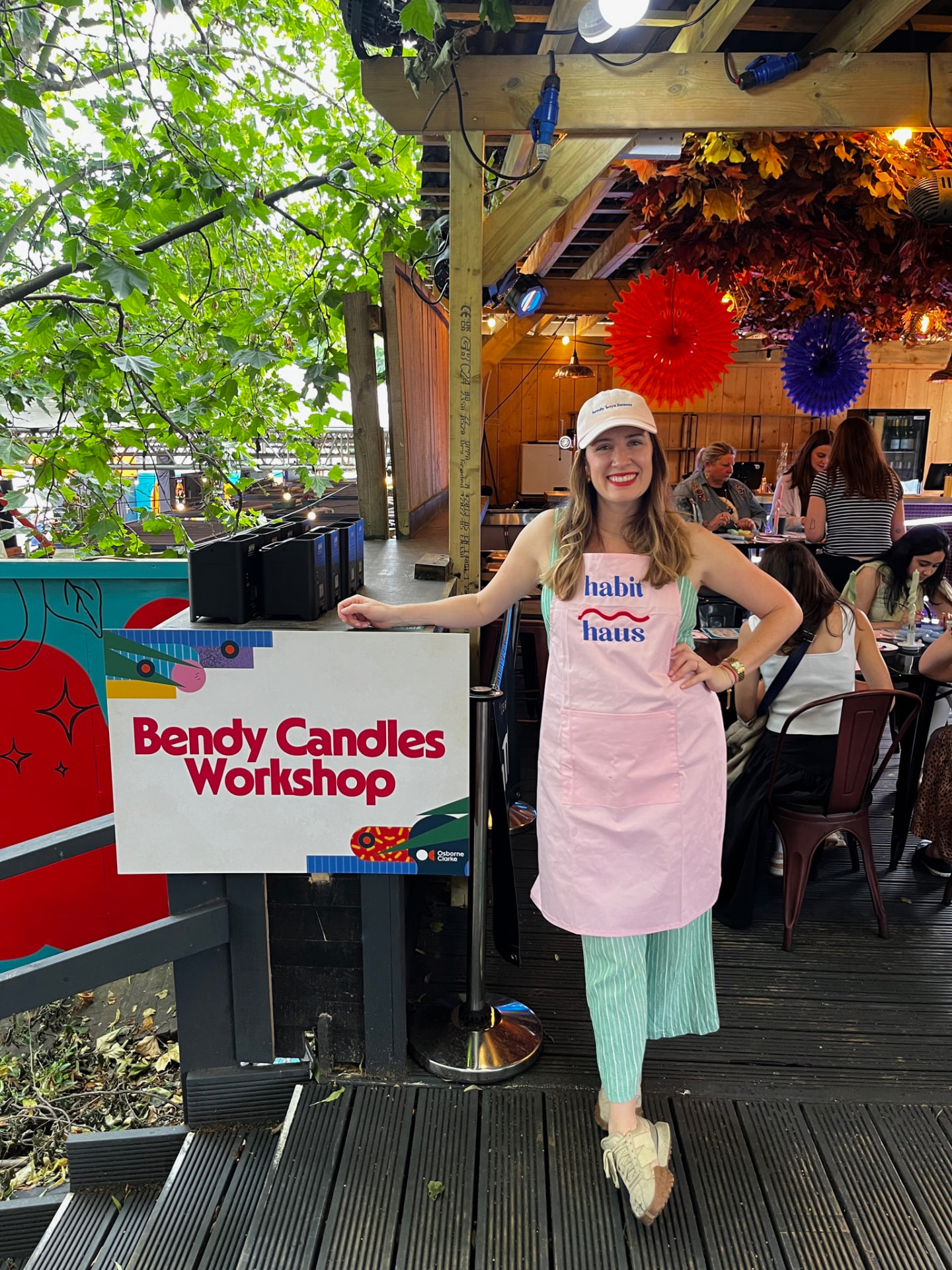 Habit Haus host in a pink apron beside a Bendy Candles Workshop sign at a corporate event
