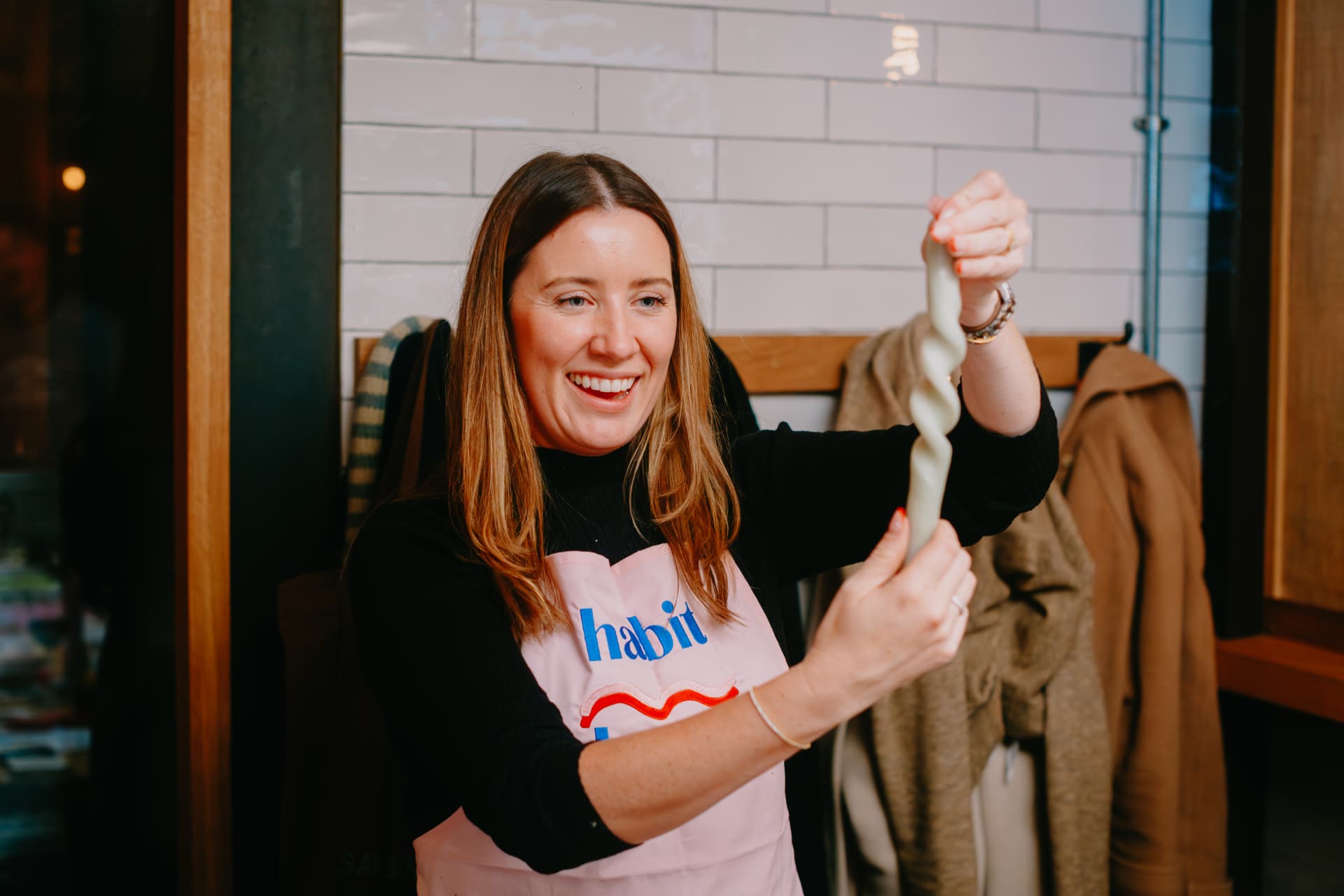 Smiling host in a Habit Haus apron bending a taper candle at a workshop