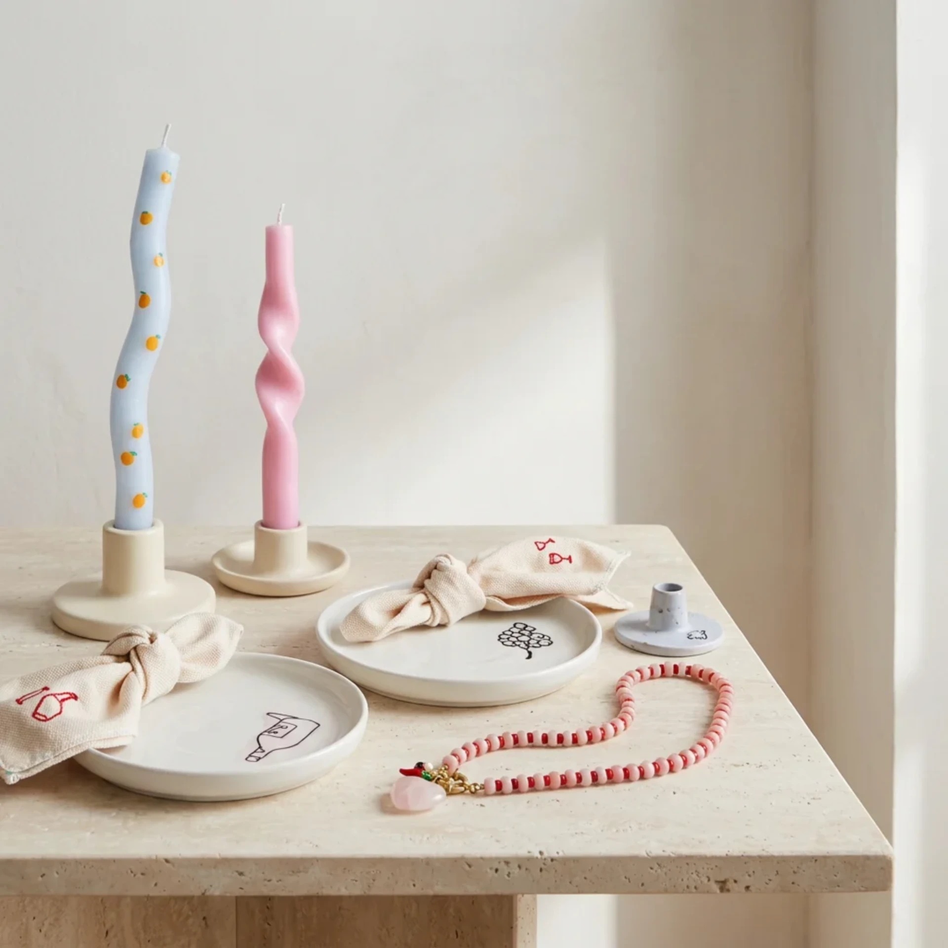Hand-bent taper candles, decorated ceramic plates and a colourful beaded necklace arranged together