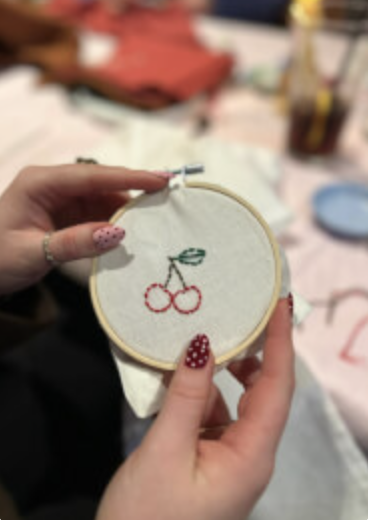 Guest stitching a cherry motif in an embroidery hoop